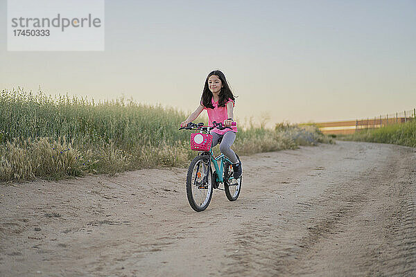 Glückliches Mädchen  das bei Sonnenuntergang auf einer Straße im Feld Fahrrad fährt
