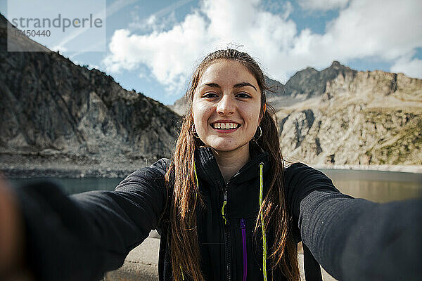 Mädchen macht ein Selfie und lächelt mit einem See im Hintergrund