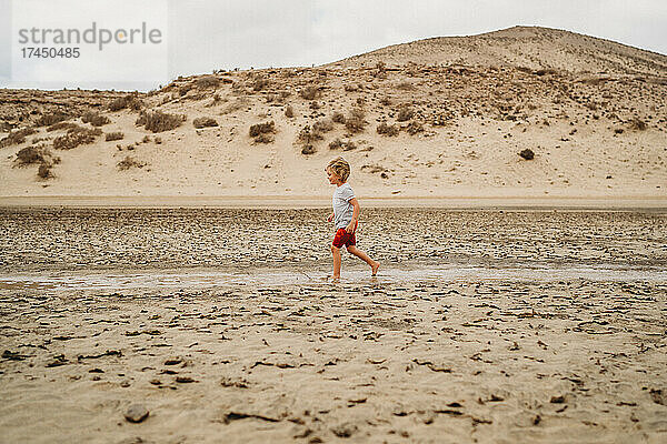 Kleines Kind läuft an bewölktem Tag zwischen Sanddünen am Strand