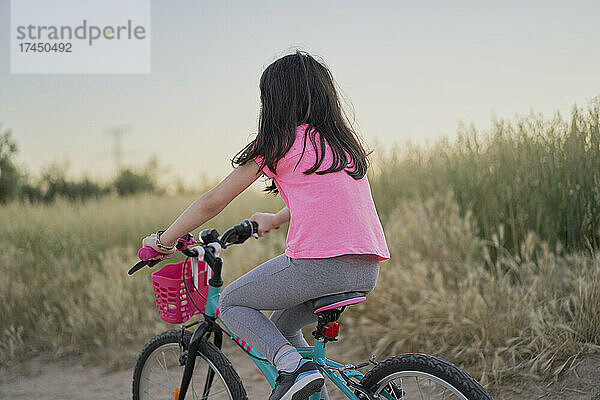 Glückliches Mädchen  das bei Sonnenuntergang auf einer Straße im Feld Fahrrad fährt