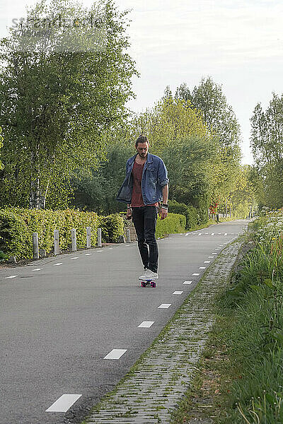 Ein Mann blickt in die Kamera  während er auf einer leeren Straße Skateboard fährt
