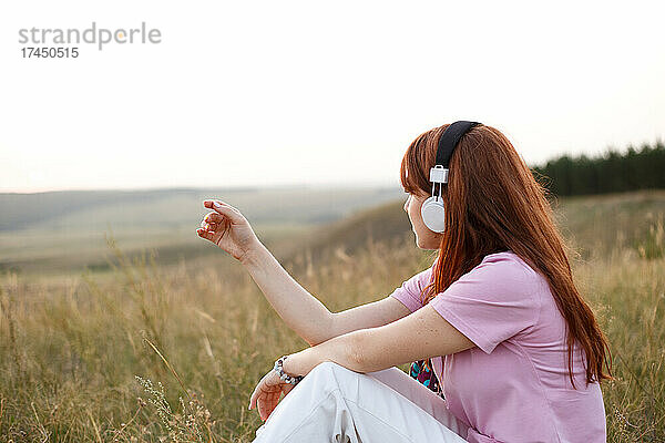 Junge rothaarige Frau mit Kopfhörern hört Musik in der Natur