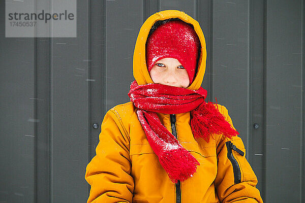 Junge in warmer Jacke und Mütze steht und schaut vor der Kamera