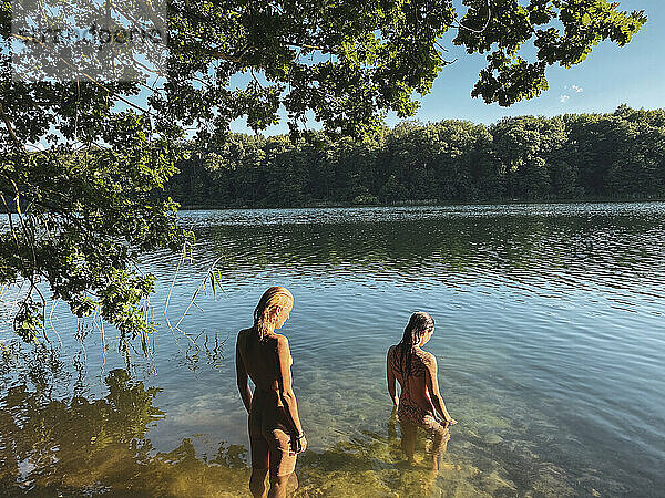 Zwei schöne natürliche Frauen stehen nackt im grünen See in Europa