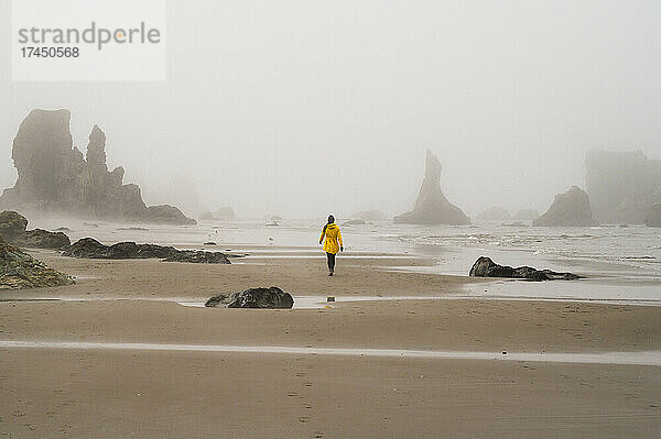 Mädchen in gelber Regenjacke spaziert am nebligen Strand von Oregon