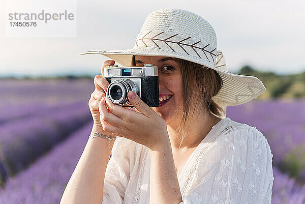 Blonde Frau macht ein Foto mit einer Vintage-Kamera in einem Lavendelfeld.