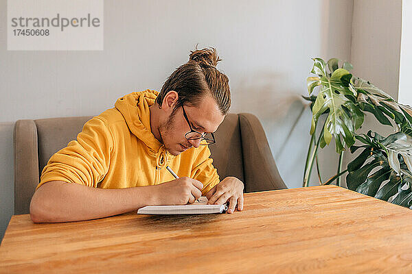 Teenager junger Mann schreibt in Notizbuch im Café. Lifestyle-Aufnahme.