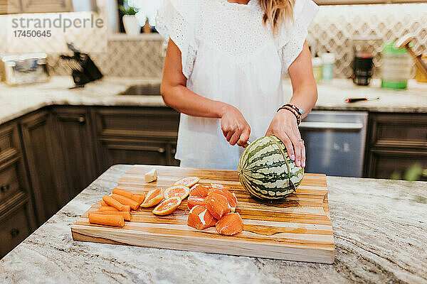 Frau schneidet Wassermelone  Orangen  Karotten und Ingwer in ihrer Küche