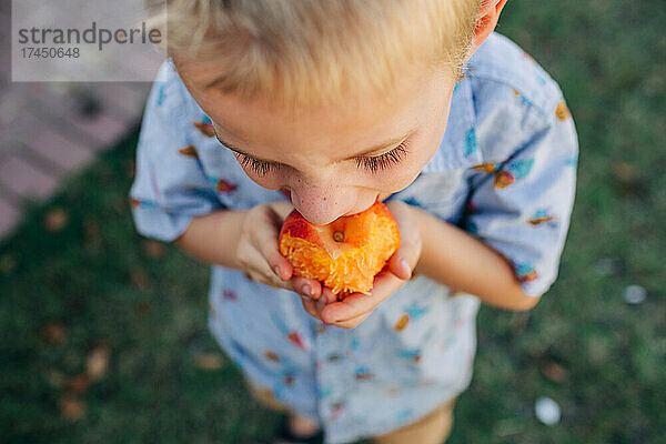 Nahaufnahme eines kaukasischen Jungen  der im Vorgarten Pfirsich isst