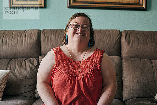 Erwachsene Frau mit Down-Syndrom lächelt und blickt zu Hause in die Kamera