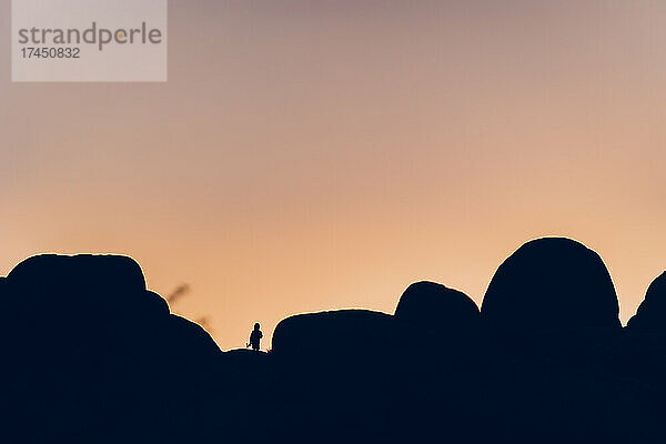 Silhouette eines Jungen zwischen Felsen bei Sonnenuntergang