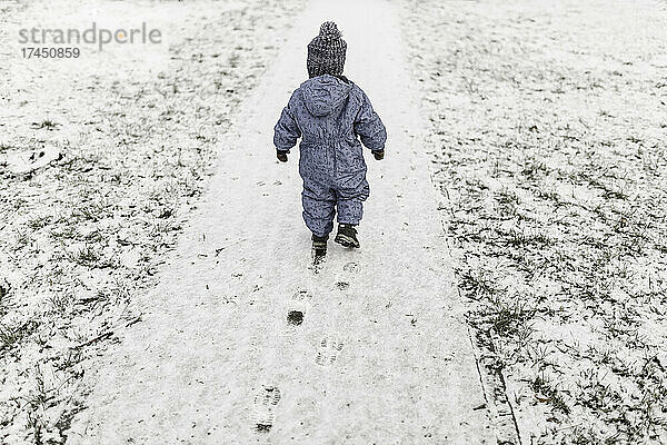 Kleiner Junge im blauen Strampler und warmer Mütze läuft auf Schnee