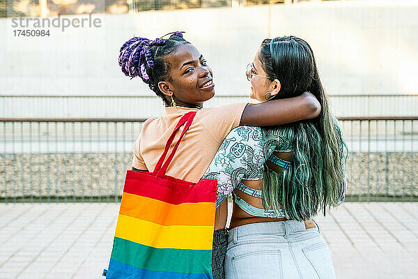 Zufriedene multiethnische lesbische Freundinnen umarmen sich auf dem Gehweg