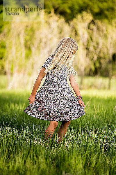 Blondes Mädchen dreht ein Kleid in einem Feld mit grünem Gras