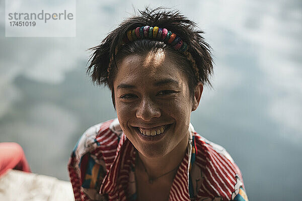 Nicht-binäre asiatische Person lächelt in buntem Hemd am See