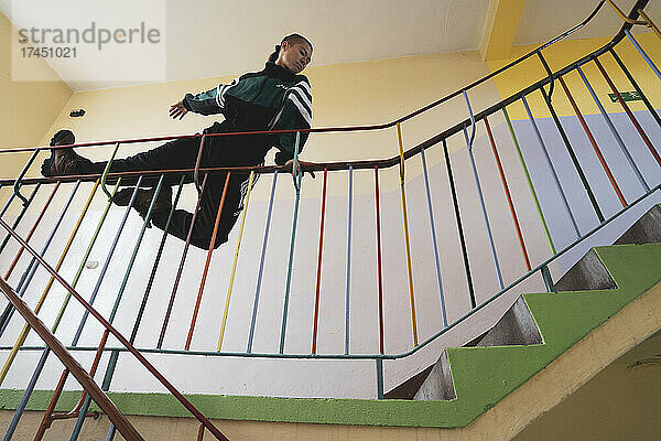 athletische androgyne starke Frau balanciert auf dem Geländer in der Farbschule