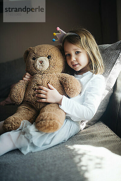 Glückliches kleines Mädchen  das zu Hause einen Teddybären umarmt.