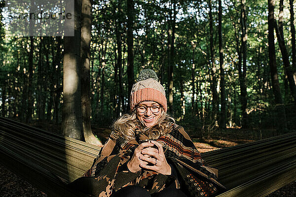Frau saß glücklich in einer Hängematte im Wald und trank Kaffee