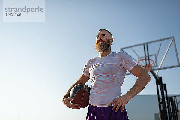 Selbstbewusster Streetballspieler vor blauem Himmel