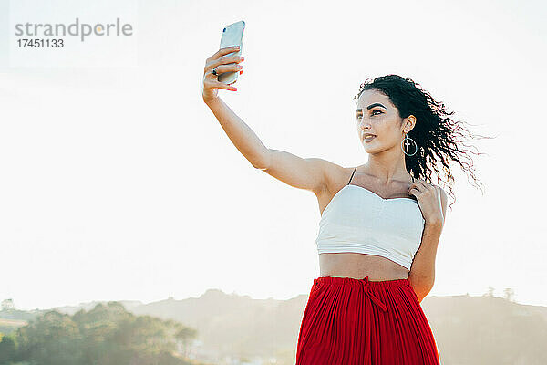 Junge Frau macht ein Selfie mit ihrem Handy und trägt ein weißes Oberteil