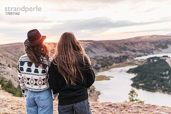 Rückansicht von zwei Frauen  die neben einem See mit Bergen stehen