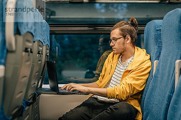 Junger Teenager mit Brille reist mit Laptop im Zug.