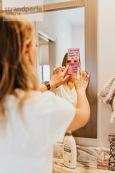 Frau liest Affirmationen vor  die an den Badezimmerspiegel geklebt sind