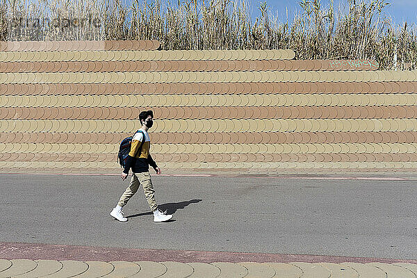 Seitenansicht eines jungen Mannes mit Rucksack und Schutzmaske beim Gehen