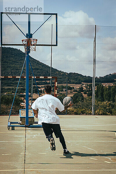 Kleiner Junge von hinten  der mit einem Basketball auf einem Platz spielt