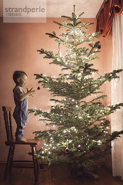 Fröhliches Kleinkind  das die ersten Weihnachtsornamente und -dekorationen anbringt