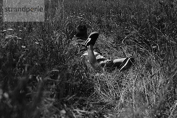 Glücklicher Junge liegt auf dem Gras in einem Sommerpark. Nettes  positives Kind