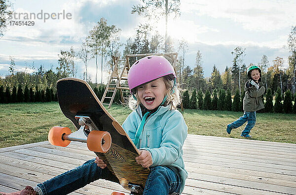 Das Mädchen saß lachend auf einem Skateboard  während ihr Bruder zu Hause spielte