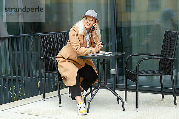 Frau kommuniziert auf einem Smartphone  das an einem Tisch auf der Terrasse sitzt