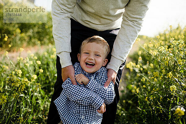 Nahaufnahme eines kleinen Jungen  der lacht  während Papa ihn im Wildblumenfeld hält