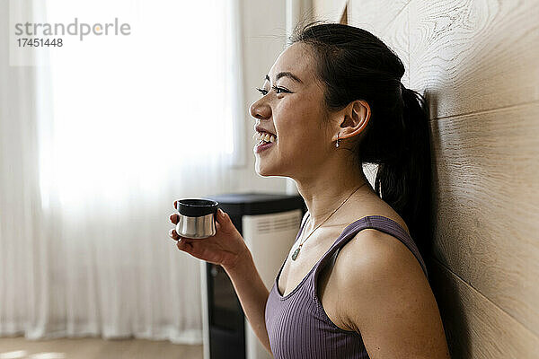 Asiatische Frau im engen Trainingsanzug hält vor dem Training Yoga-Tee in der Hand
