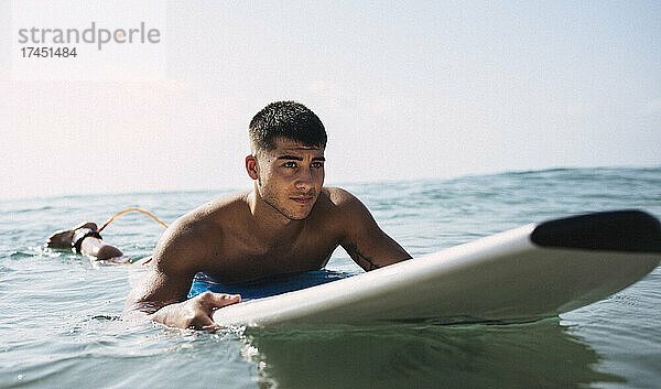 Junger brünette Surfer wartet auf seinem Brett im Meer auf eine Welle.