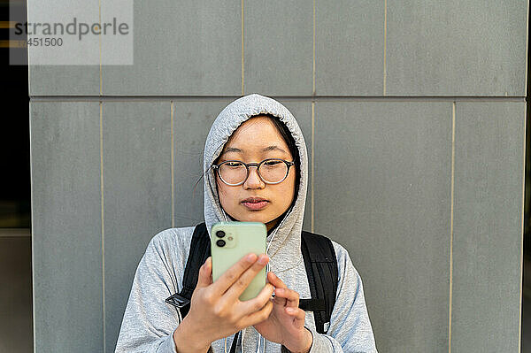 Junger asiatischer Erwachsener benutzt Mobiltelefon und trägt eine Brille