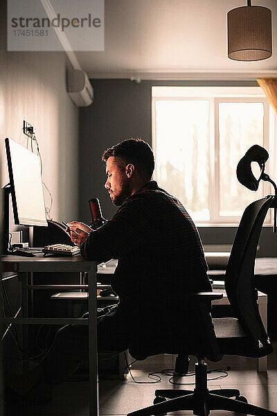 Mann benutzt Smartphone und Computer  sitzt am Schreibtisch und arbeitet zu Hause