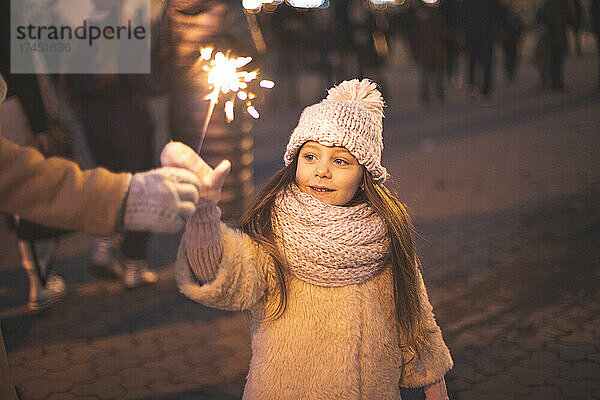 Kleines Mädchen geschmückt mit Licht und hält brennende Funken in der Hand