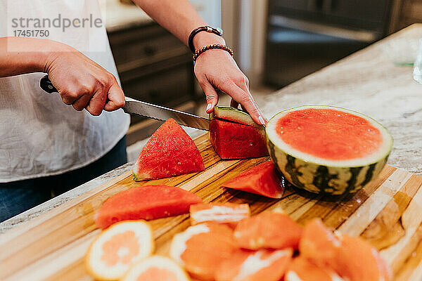 Nahaufnahme einer Frau  die in ihrer Küche Wassermelone und andere Früchte schneidet