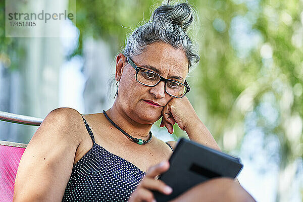 Frau mittleren Alters im Badeanzug liest entspannt ein E-Book