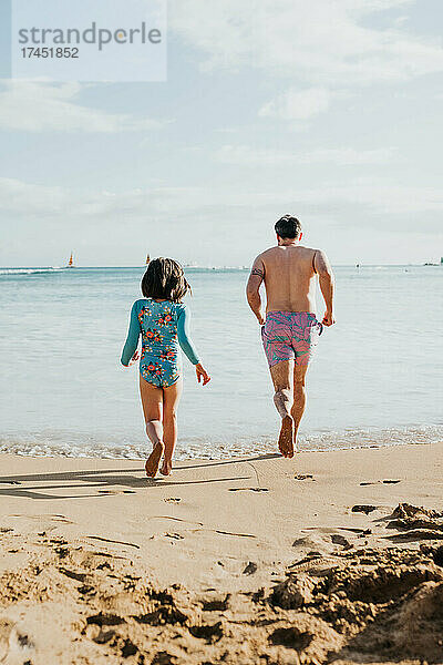 Vater und Tochter laufen und spielen im Meer am Strand von Waikiki