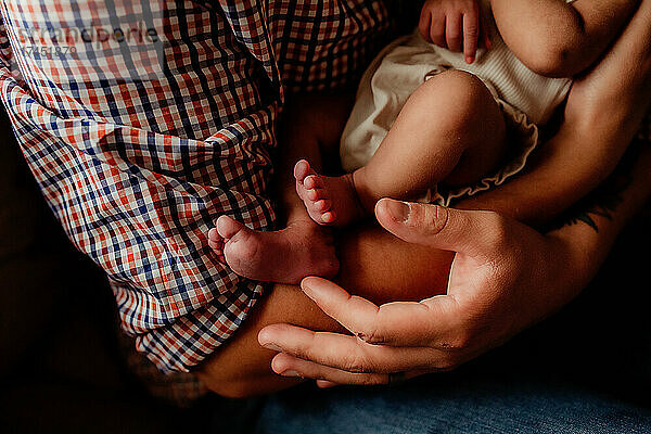 Detailaufnahme der Zehen des Babys und der Hände des Vaters.