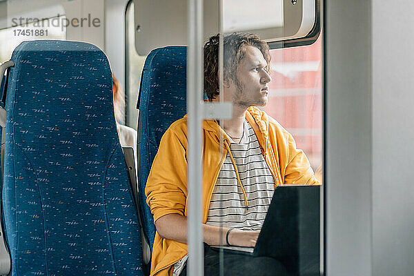 Junger Mann  Teenager  der aus dem Fenster schaut und am Laptop arbeitet.
