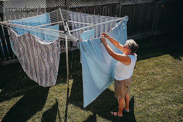 Ältere Frau hängt Wäsche an einer Wäscheleine im Freien auf.