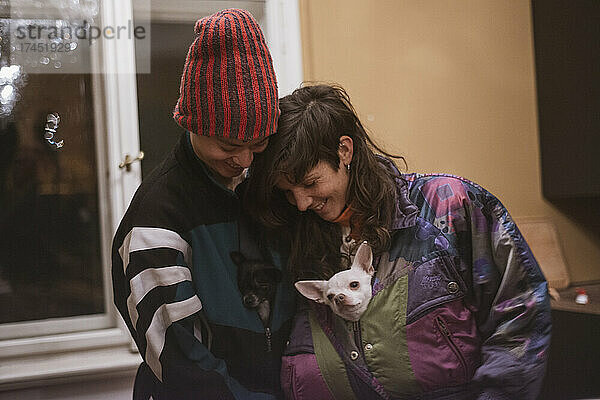 sweet female queer couple cuddle with cute chihuahua dogs in snowcoats