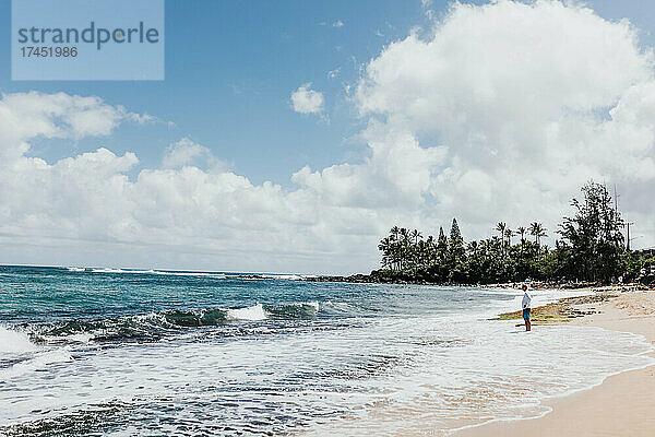 Mann steht an einem Strand auf Oahu und beobachtet die hereinbrechenden Wellen