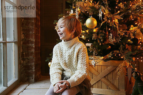 Nahaufnahme eines lächelnden Kindes neben einem Weihnachtsbaum.