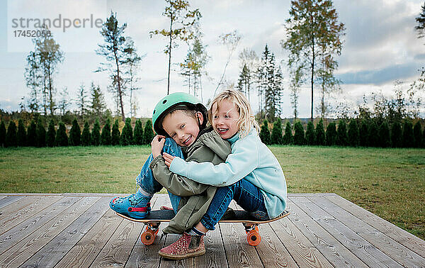Bruder und Schwester umarmen sich auf einem Skateboard und spielen im Garten