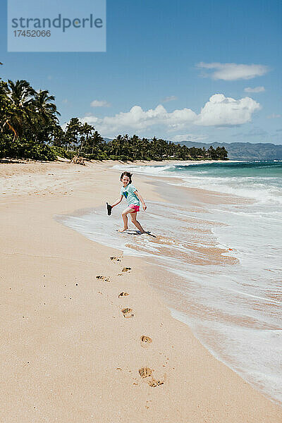 Junges Mädchen rennt vor den Wellen am Strand von Oahu davon